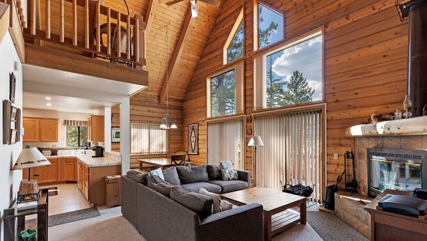 A spacious living area with a large sofa, a fireplace, and a kitchen in the background. - Lake View Mountain Cabin (June Lake)