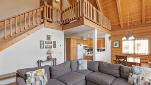 A spacious living area with a gray sectional sofa, wooden staircase, and a kitchen in the background. - Lake View Mountain Cabin (June Lake)