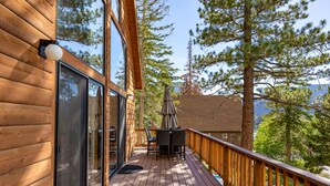 A wooden deck with a glass door, outdoor furniture, and a view of trees and mountains. - Lake View Mountain Cabin (June Lake)
