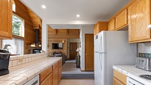 A kitchen with wooden cabinets, a white refrigerator, a stove, and a large window. - Lake View Mountain Cabin (June Lake)