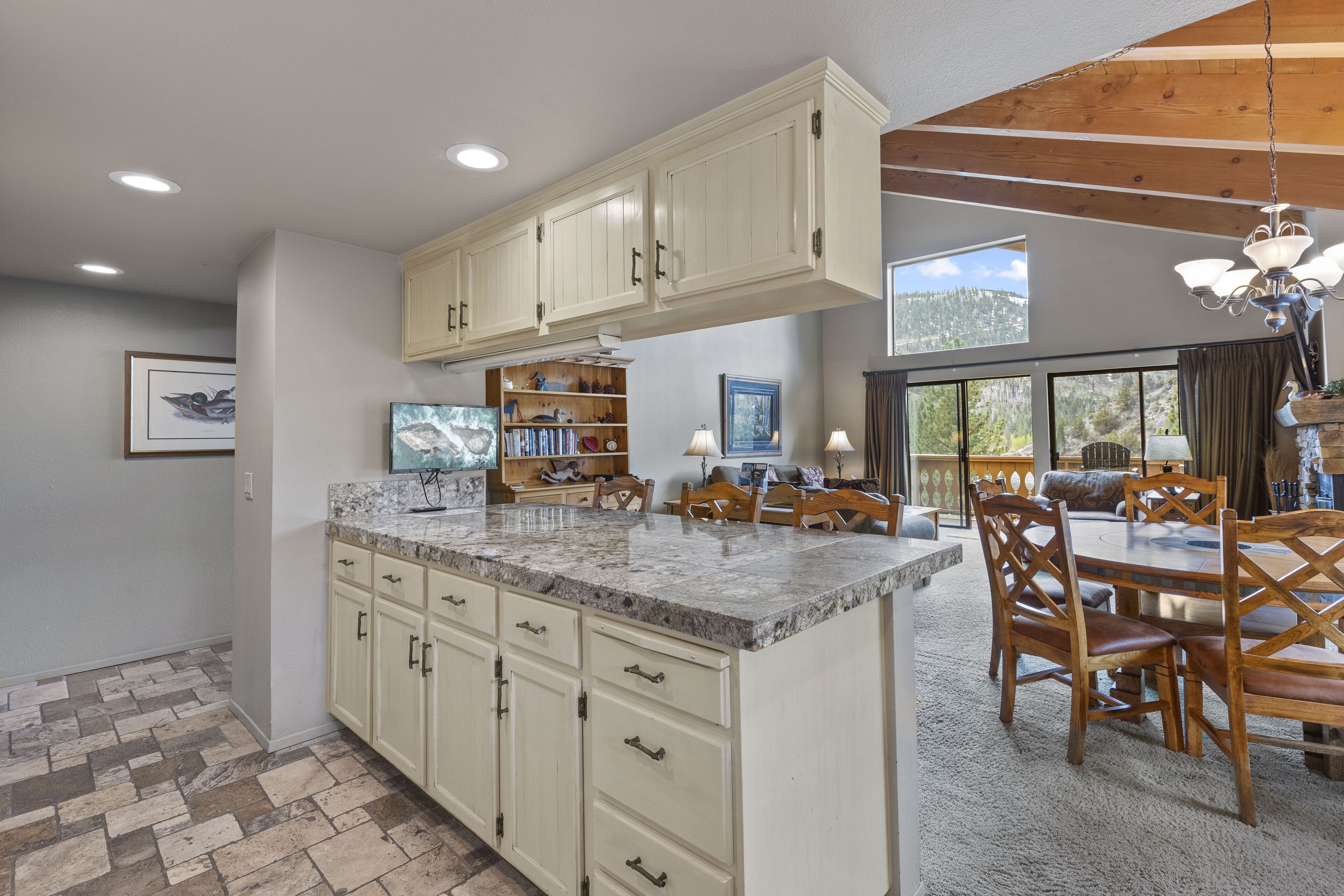 A spacious kitchen with white cabinets, a granite countertop, and a dining area with wooden chairs and a chandelier.