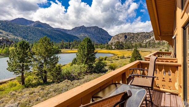 A wooden deck with a table and chairs overlooking a lake and mountains.