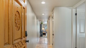 A hallway with a wooden door on the left, a white door on the right, and a tiled floor.