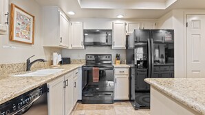 A modern kitchen with white cabinets, a black stove, a microwave, and a refrigerator.