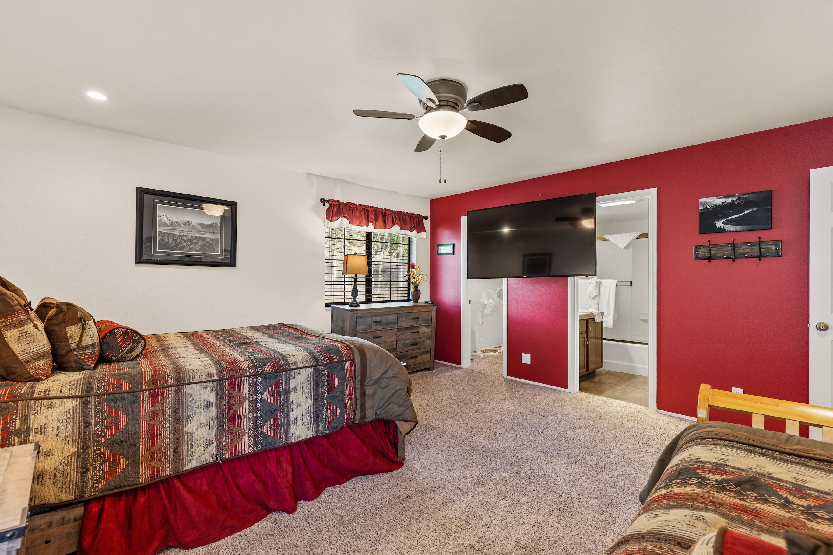 Une chambre à coucher avec un lit, un ventilateur de plafond, une commode et un mur rouge.