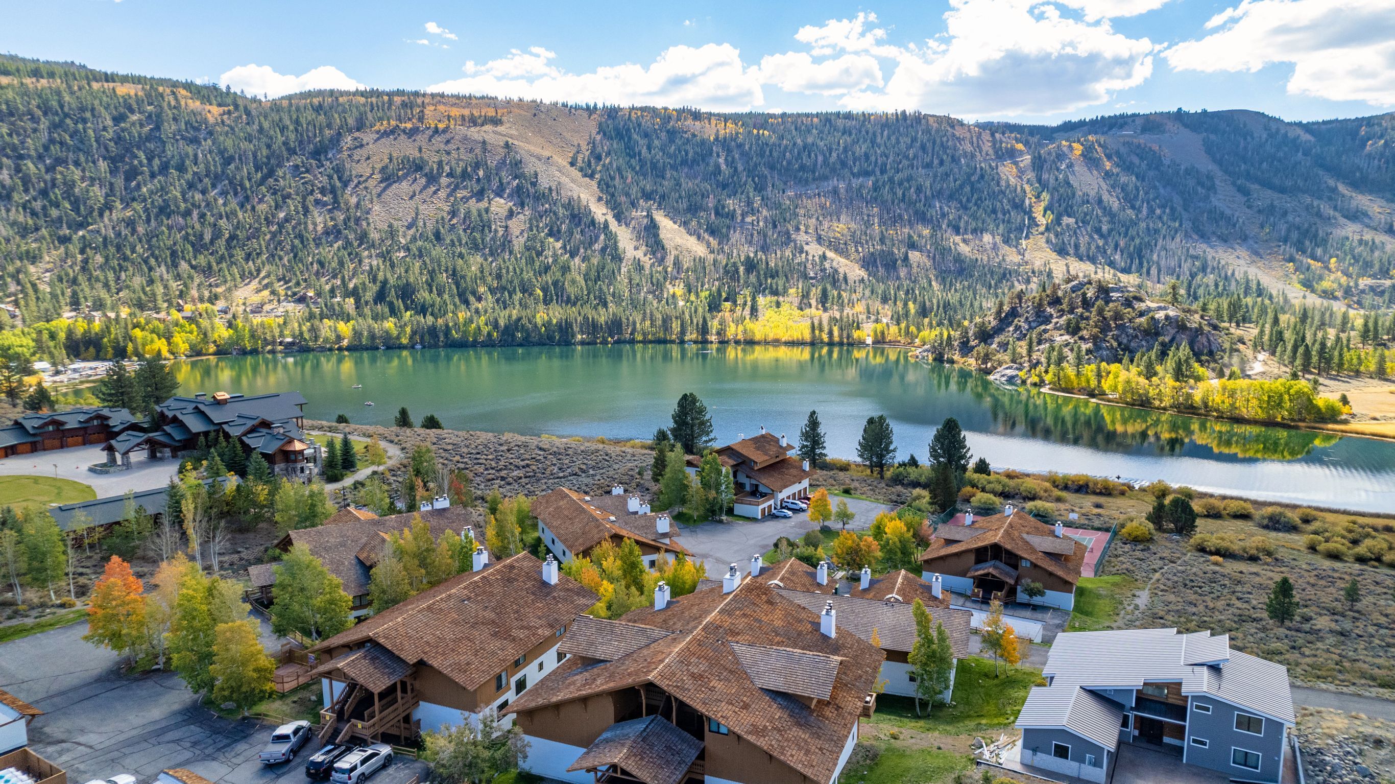 Un complexe hôtelier au bord d’un lac, avec des chalets, une piscine et une vue sur le lac et les montagnes.