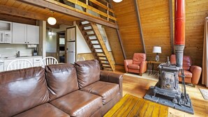 Une pièce confortable de style loft, avec un canapé en cuir marron, un escalier en bois et un poêle à bois d'époque.