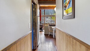 Un couloir étroit, doté de planchers et de murs en bois, mène à un coin repas où se trouvent une table et des chaises.