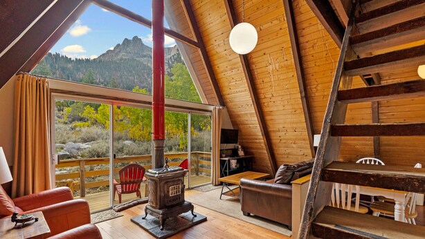 Un chalet confortable avec un intérieur en bois, une grande fenêtre donnant sur les montagnes, un fauteuil rouge et une cheminée.