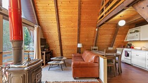 A cozy cabin interior with a wooden ceiling, a fireplace, a sofa, a dining table, and a kitchen area. - Four Seasons Cabin 2 (June Lake)