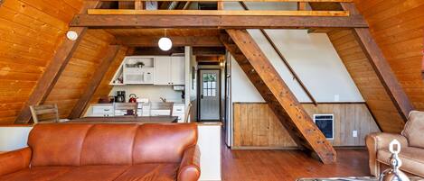 An attic bedroom with a sloped ceiling, wooden beams, a brown leather sofa, and a metal decorative piece.