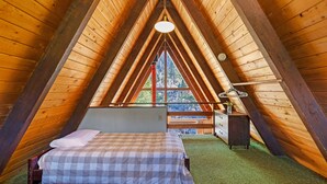 A cozy attic bedroom with a checkered bed, a small desk, and a view of the outdoors through a large window. - Four Seasons Cabin 2 (June Lake)