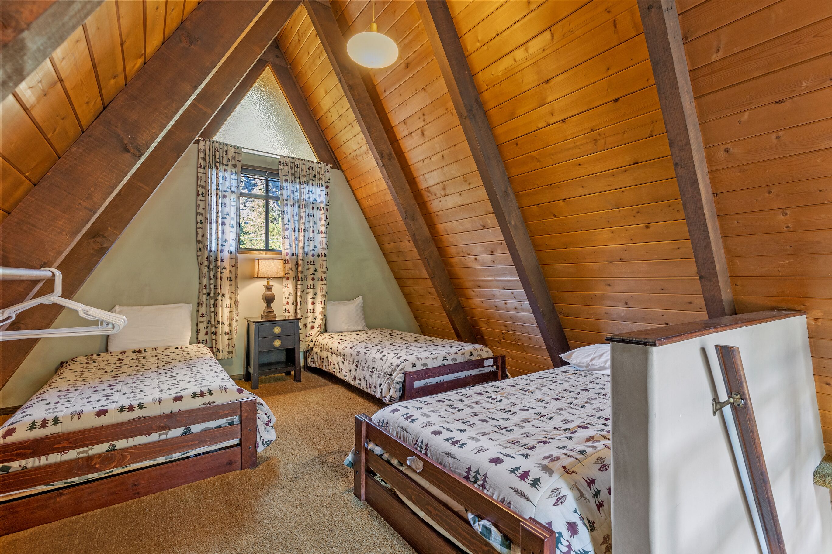 A cozy attic bedroom with two wooden beds, a small table, and a hanging light fixture.