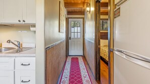 A narrow hallway with wooden flooring, a red patterned carpet, a sink, cabinets, and a refrigerator.