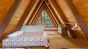 A cozy attic bedroom with a sloped ceiling, a bed with patterned bedding, a dresser, and a window offering a view of trees.