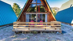 A wooden A-frame cabin with a balcony and two chairs.