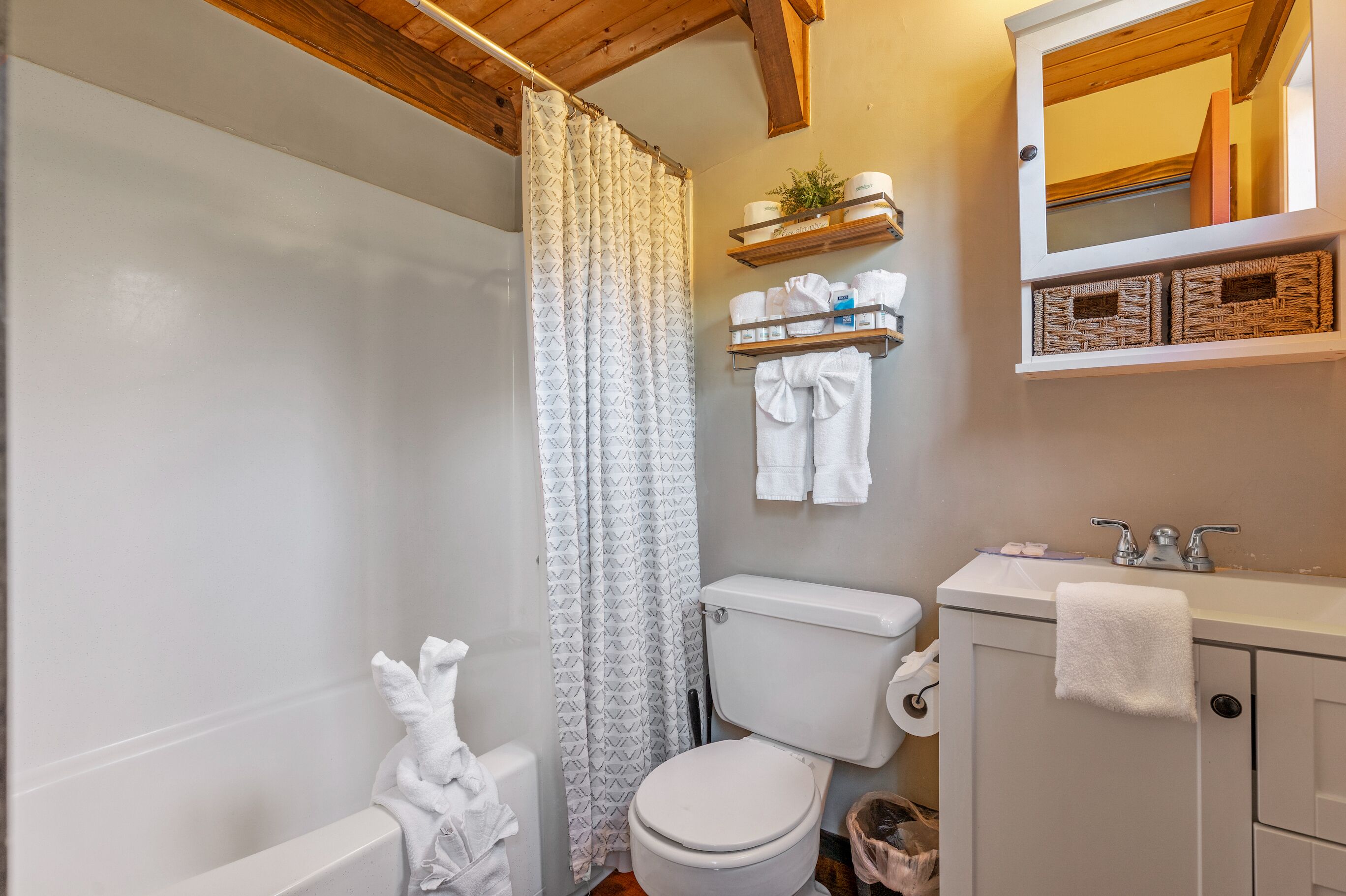 Une salle de bain avec des toilettes, un lavabo et un rideau de douche. Des serviettes sont accrochées au mur et une étagère contient des articles de toilette.
