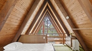 A bedroom with a wooden sloped ceiling, a bed with white bedding, a dresser, and a radiator. - Four Seasons Cabin 5 (June Lake)