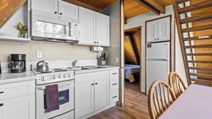 A compact kitchen with white cabinets, a stove, a microwave, and a refrigerator. - Four Seasons Cabin 5 (June Lake)