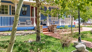 Une maison à l’extérieur bleu, avec un porche à l’avant doté de marches et un jardin agrémenté d’un muret en pierre et d’un arbre.