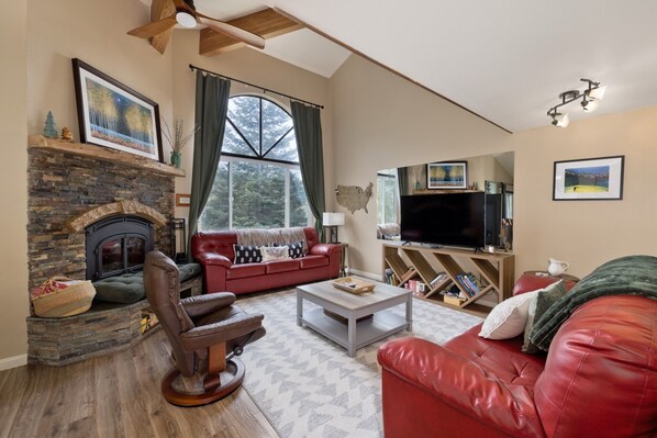 A living room with a fireplace, red leather sofa, a television, and a large window with curtains. - Edgewater 19, steps from the June Lake Marina. (June Lake)