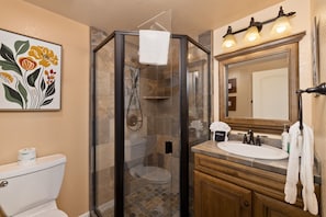 A bathroom with a glass-enclosed shower, a toilet, a sink, and a mirror.