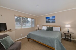 A bedroom with a bed, a television, a window with blinds, a painting, and two bedside tables with lamps. - Edgewater 19, steps from the June Lake Marina. (June Lake)