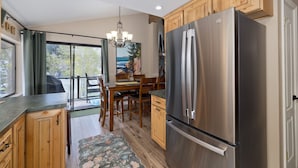 A kitchen with wooden cabinets, a stainless steel refrigerator, a dining table with chairs, and a chandelier. - Edgewater 19, steps from the June Lake Marina. (June Lake)