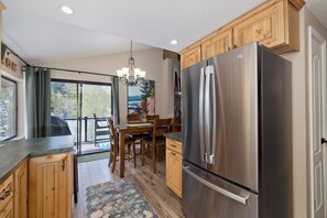 A kitchen with wooden cabinets, a stainless steel refrigerator, a dining table with chairs, and a chandelier.