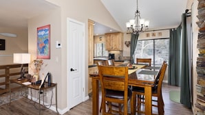 A dining area with a wooden table and chairs, a chandelier, and a view of the kitchen. - Edgewater 19, steps from the June Lake Marina. (June Lake)