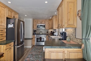A kitchen with wooden cabinets, a stainless steel refrigerator, a microwave, a stove, and a sink.