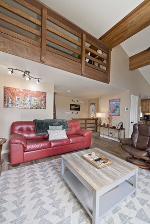 A spacious living area with a red leather couch, a wooden coffee table, and a high ceiling with exposed beams. - Edgewater 19, steps from the June Lake Marina. (June Lake)