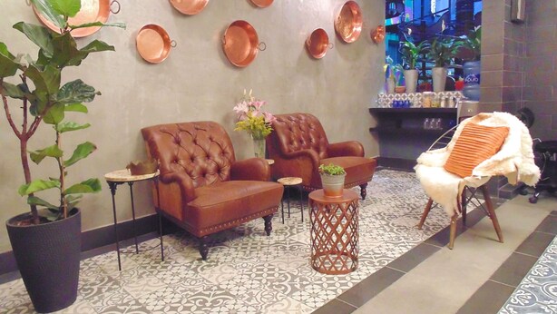 A lobby with a patterned floor, two brown leather sofas, a white chair, a small round table with a plant, and copper plates on the wall. - Suites Viveros de Coyoacan (Mexico City)