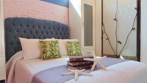 A bedroom with a tufted headboard, a bed with a white and purple bedspread, two pillows with leaf patterns, a stack of books, and a white starfish decoration. - Suites Viveros de Coyoacan (Mexico City)