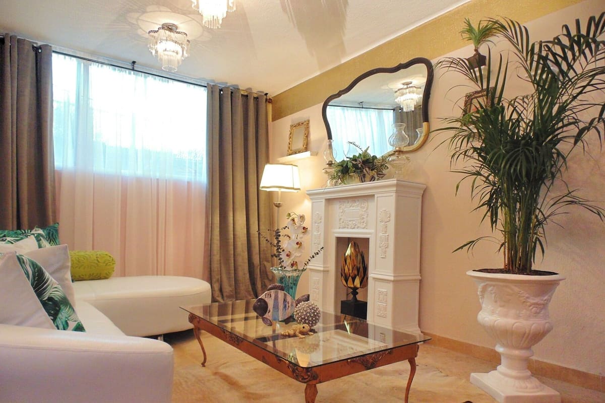 A living room with a glass coffee table, white sofa, and a large potted plant.