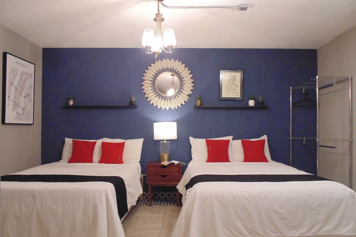 A hotel room with two beds, a chandelier, a mirror, and shelves with decorative items.