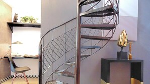 A spiral staircase with a metal railing, a desk with a plant, and a chair in a room with patterned floor tiles. - Suites Viveros de Coyoacan (Mexico City)