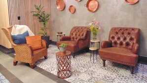 A lobby with a seating area featuring two leather armchairs, a wicker chair, and a small round table with a vase of flowers. - Suites Viveros de Coyoacan (Mexico City)