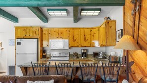 Une cuisine avec des meubles de rangement en bois, un réfrigérateur, un four à micro-ondes, une cuisinière et des tabourets de bar.