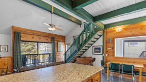Une cuisine dotée d’un plan de travail en granit, de meubles en bois, d’un coin repas avec une table et des chaises, d’un escalier et offrant une vue sur l’extérieur grâce à de grandes fenêtres.