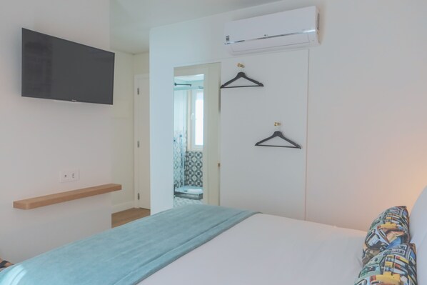 A bedroom with a bed, a TV mounted on the wall, a wardrobe with two hangers, and a hallway leading to a bathroom.