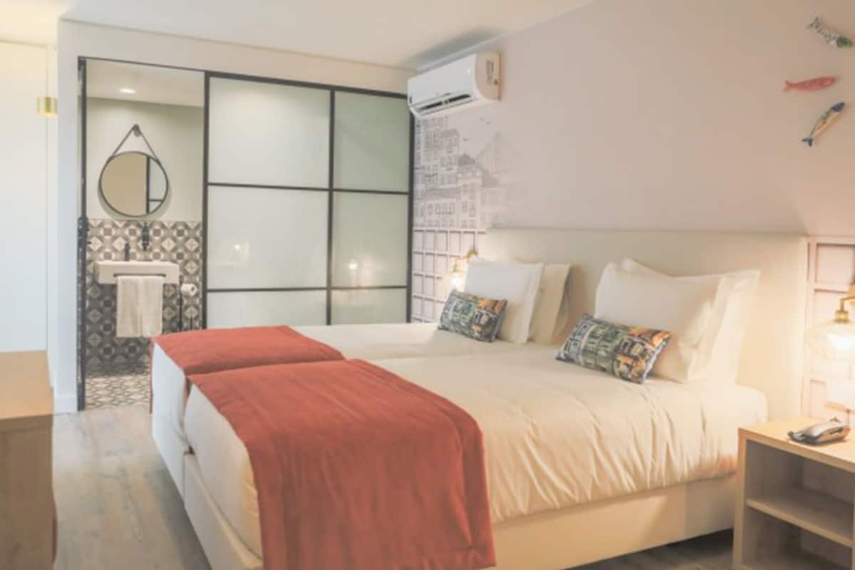 Habitación de hotel con una cama grande, una mesita de noche, un espejo, un aire acondicionado de pared y un pequeño estante.