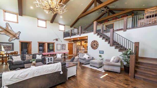 A spacious living room with a high ceiling, wooden beams, a staircase, and a dining area. - Red Barn Retreat in the Heart of Bloomington  (Bloomington)