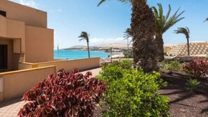 A modern building with a pool area, palm trees, and a view of the sea. - Home2book Sea Front El Granillo, Beach & Wifi (Costa Calma)