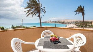 A balcony with a table and chairs, overlooking a coastal view with palm trees and a clear sky. - Home2book Sea Front El Granillo, Beach & Wifi (Costa Calma)