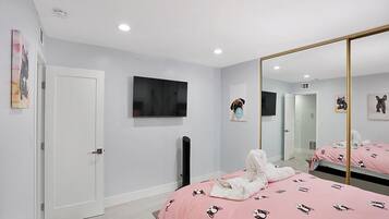 A bedroom with a bed covered in pink bedding with dog prints, a large mirror, and a flat-screen TV mounted on the wall.