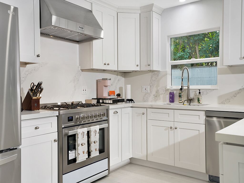 Cocina moderna con armarios blancos, estufa de acero inoxidable y ventana con vistas a la vegetación.