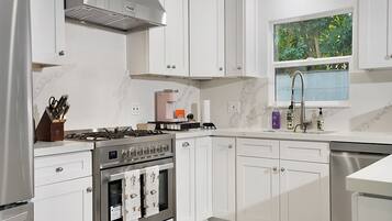 Cocina moderna con armarios blancos, estufa de acero inoxidable y ventana con vistas a la vegetación.