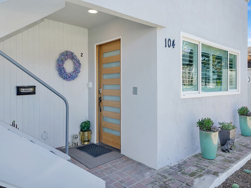 A house with a wooden door, a number '104' on the wall, and potted plants outside.