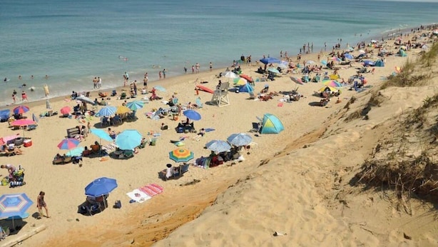 Una playa concurrida, con muchos sombrillas y sillas de playa.